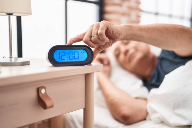 istock Middle age grey-haired man lying on bed turning off alarm clock at bedroom 1446459911