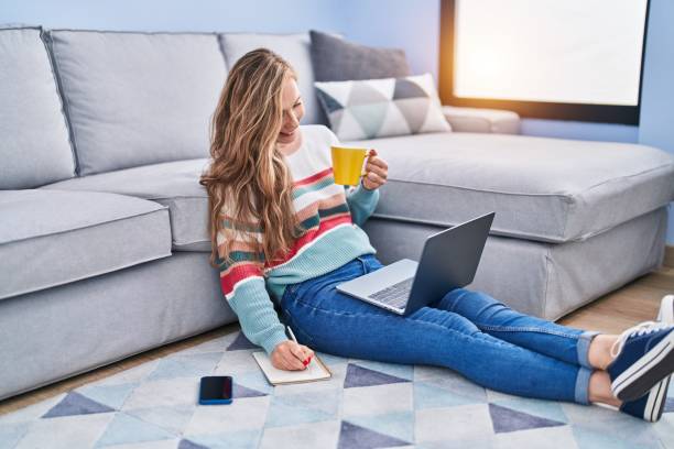 istock Young blonde woman using laptop writing on notebook at home 1446460271