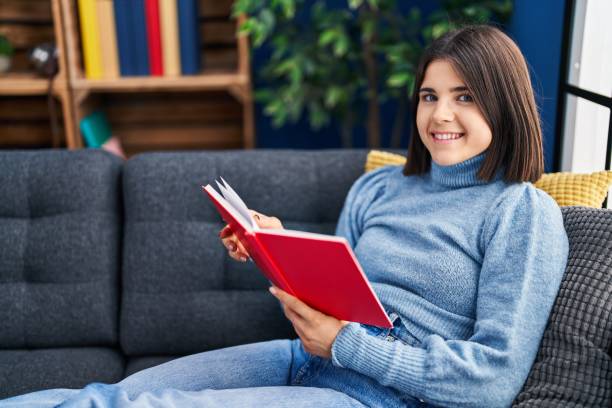 istock Young beautiful hispanic woman reading book sitting on sofa at home 1446460480