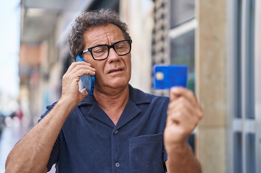 Middle age man talking on smartphone and credit card at street