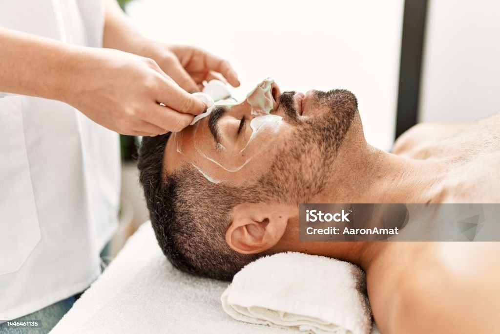 Young hispanic man having facial mask treatment at beauty center Facial Mask - Beauty Product Stock Photo