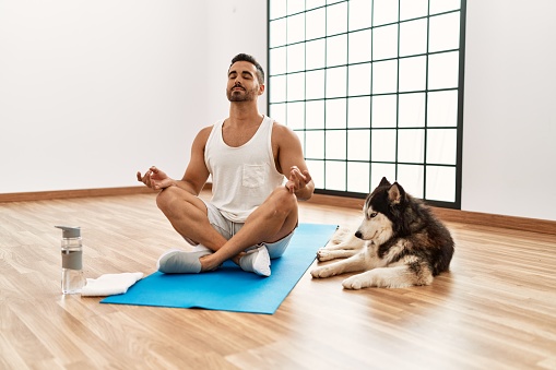 Young hispanic man training yoga with dog at sport center