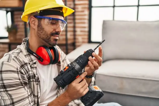 Photo of Young hispanic man worker smiling confident holding drill at home