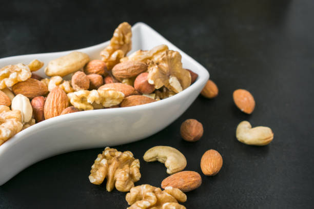 istock Assorted nuts in white shape bowl on black background. Healthy vegan diet 1446464428