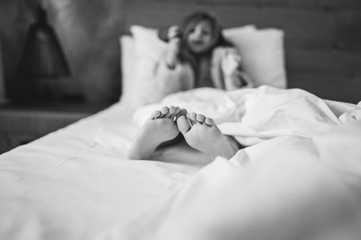 Black and white shot of one cute little girl sitting in bed and brushing her hair, focus on feet