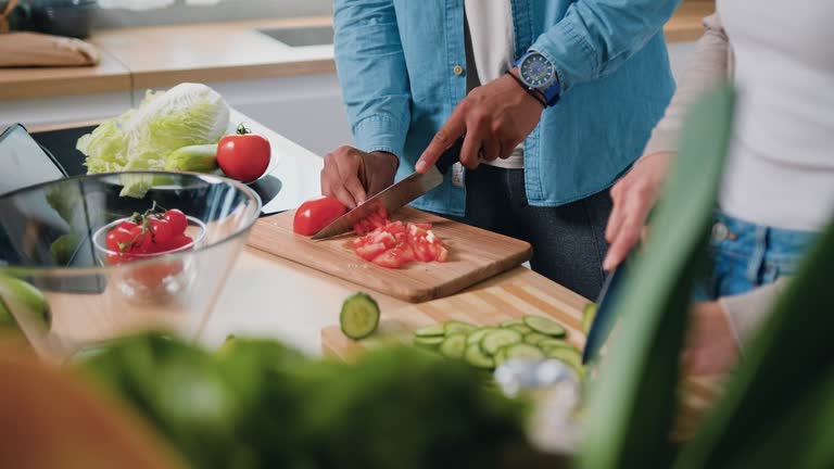 Close-up. Male hands cutting tomatoes with knife in kitchen while man is cooking salad from fresh raw vegetables. Healthy food concept.