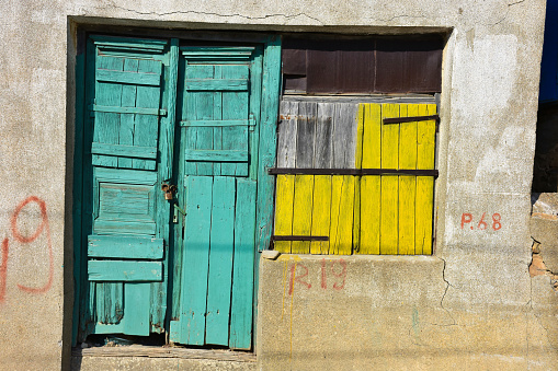 old green wooden door, wooden yellow window of an abandoned greek town home
