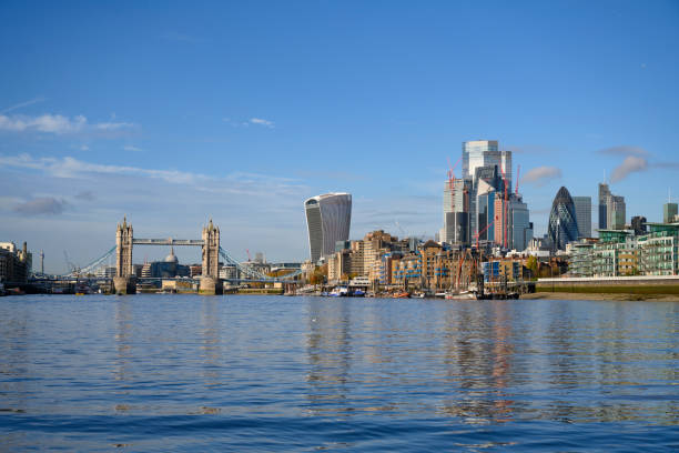 Sunny wide angle view above River Thames of Tower Bridge, riverfront, and financial district with iconic skyscrapers and cranes amidst construction development.