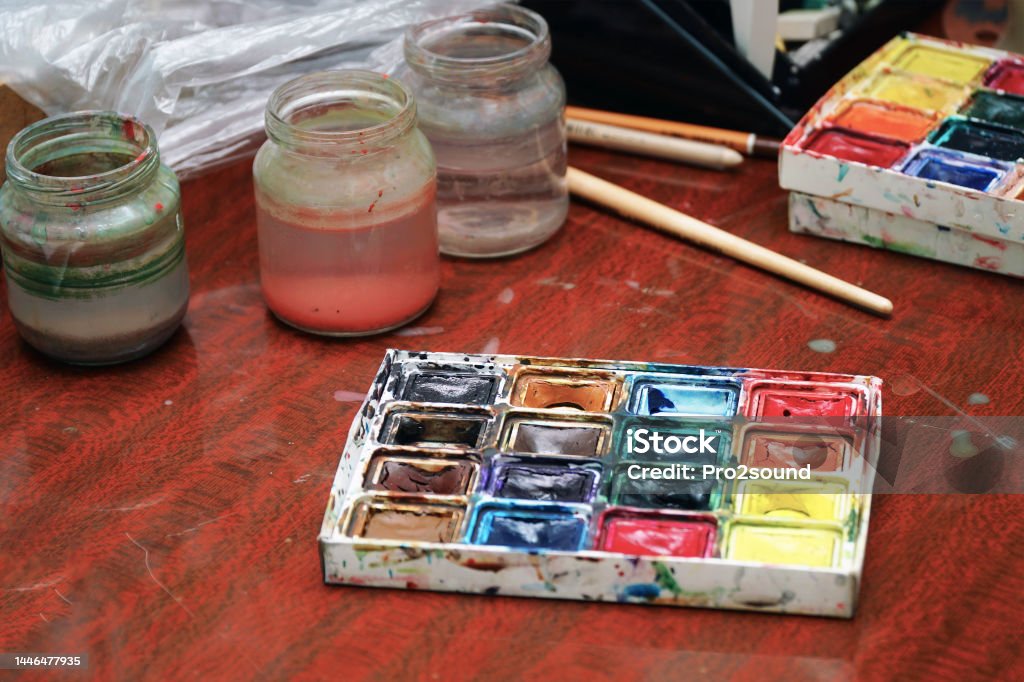 Watercolor paints, a paint brush and jars of water on the table Watercolor paints, a paint brush and jars of water on the table. Selective focus Art Stock Photo
