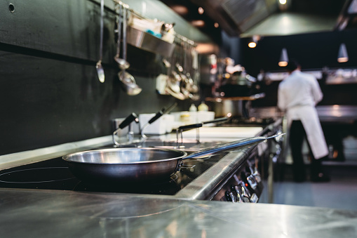 A chef is preparing food in the restaurant's kitchen. Selective focus on a pan on the stove.