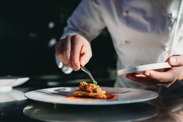 ein koch beendet die zubereitung des tellers - essen am tisch stock-fotos und bilder