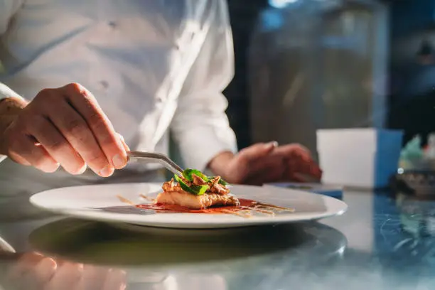 A chef is finishing the preparation of the plate. He's decorating the plate just before the serving.