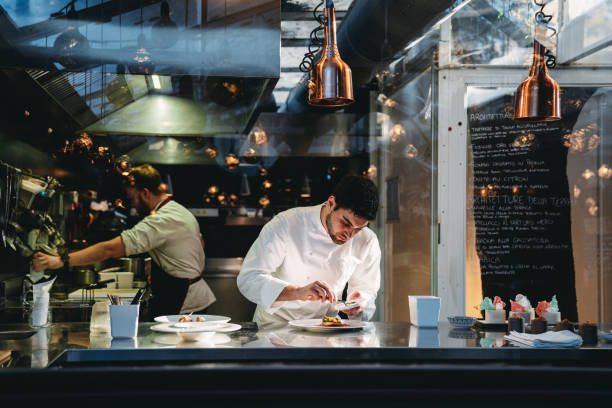 A chef is cooking in his restaurant's kitchen A chef is cooking in his restaurant's kitchen. Shot through the glass. High-end gourmet restaurant. restaurant kitchen workers stock pictures, royalty-free photos & images