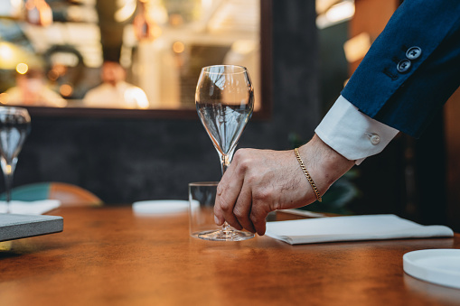 A waiter is setting the table before the arrive of the clients. High-end luxury restaurant.