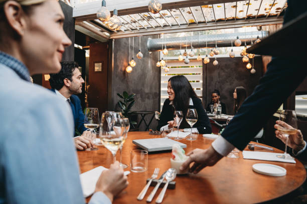 Colleagues are enjoying a meal at the restaurant during a meeting Colleagues are enjoying a meal at the restaurant during a meeting. Elegant high-end restaurant. A waiter is serving them. formal dinning stock pictures, royalty-free photos & images