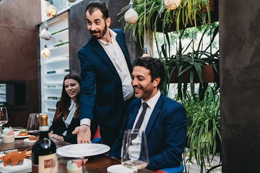 A waiter is serving food in an high-end restaurant. Business people meeting at the restaurant.