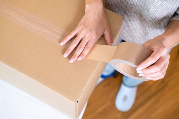 Top down view on a woman taping cardboard box in the kitchen.