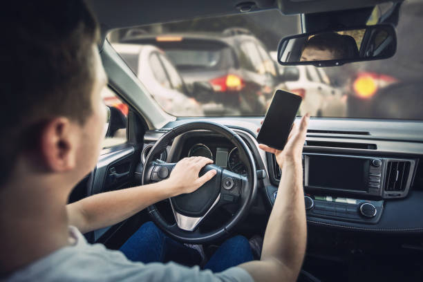 conductor furioso tocando la bocina del auto enojado por el atasco de tráfico que se avecina. chico agresivo conduce inseguro mientras usa su teléfono frente al volante, violando las reglas - driving car distracted accident fotografías e imágenes de stock