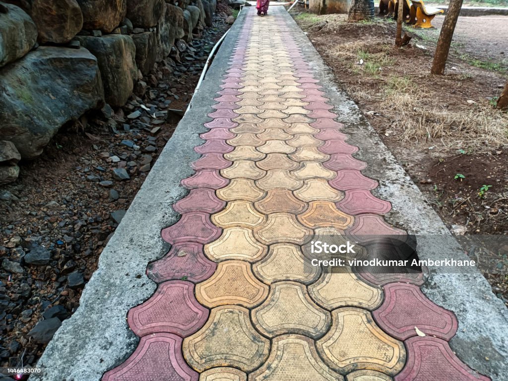 Stock photo of red and yellow color interlocking concrete paver blocks pathway in the public garden, Picture captured early in the morning at Kolhapur, Maharashtra, India. focus on object. Angle Stock Photo