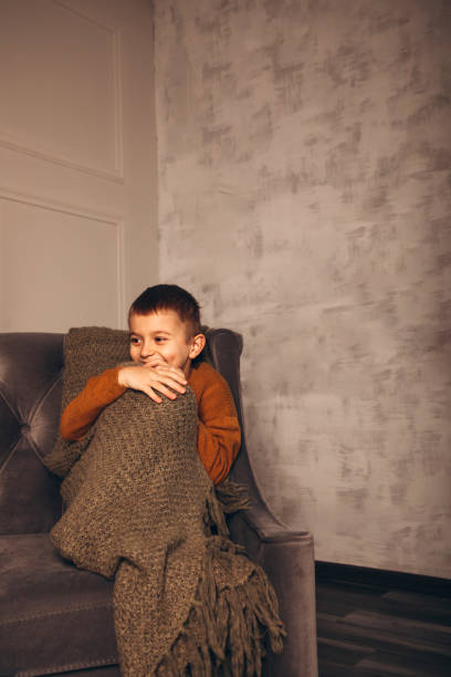 Portrait of a boy sitting on a sofa. Boy covered with a blanket smiling stock photo