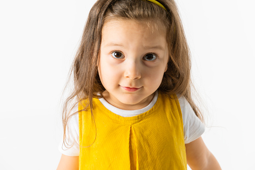 Cute little girl in a yellow dress is looking at camera with a cute smile.