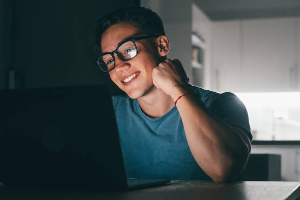 istock One young teenager studying and working at home at night on the table using laptop pc smiling and having fun doing homework. Light of screen on face. 1446489989