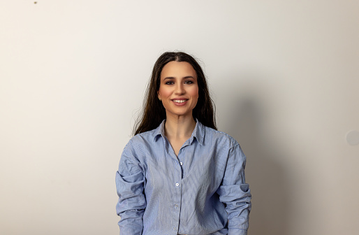 A portrait of an attractive woman in a fashion studio smiling in front of a wall.