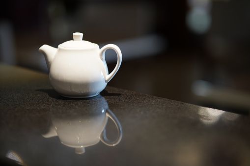 White ceramic teapot for brewing tea on a black background with reflection