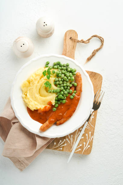 bangers und brei. grillwürstchen mit kartoffelpüree und grünen erbsen auf weißem teller auf hellem hintergrund. traditionelles gericht aus großbritannien und irland. bbq rindfleischwürste. draufsicht. - mashed potato food staple vertical color image stock-fotos und bilder