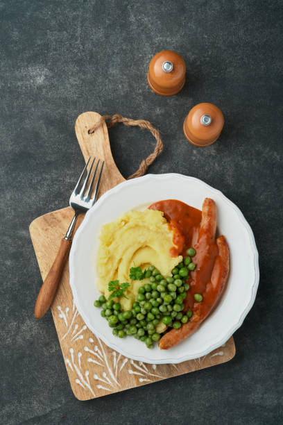 bangers und brei. gegrillte würstchen mit kartoffelpüree und grünen erbsen auf weißem teller auf schwarzem dunklem hintergrund. traditionelles gericht aus großbritannien und irland. bbq rindfleischwürste. draufsicht. - mashed potato food staple vertical color image stock-fotos und bilder