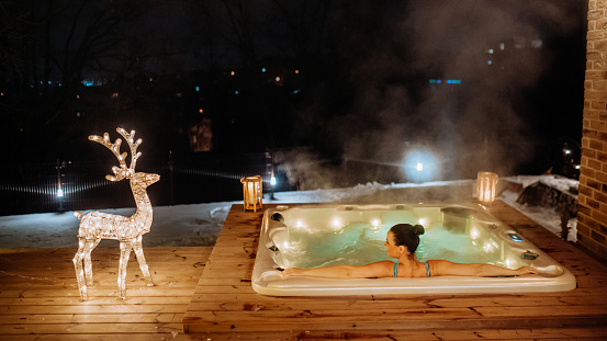 Young woman enjoying outdoor bathtub in her terrace during a cold winter evening.