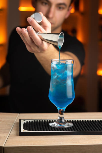 istock Professional male bartender pouring a blue alcoholic drink from the jigger on cocktail glass, preparing Blue Lagoon cocktail 1446499683