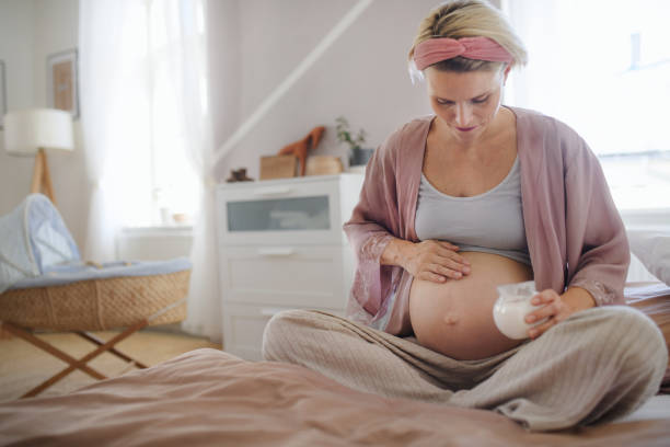 Pregnant woman creaming her belly, taking care of herself. Pregnant woman creaming her belly,sitting in a bed, taking care of herself. creaming stock pictures, royalty-free photos & images