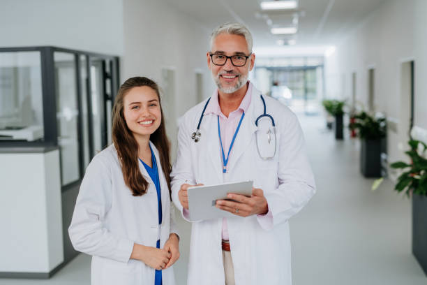 Portrait of elderly doctor with his younger colleague at hospital corridor. Health care concept. stock photo
