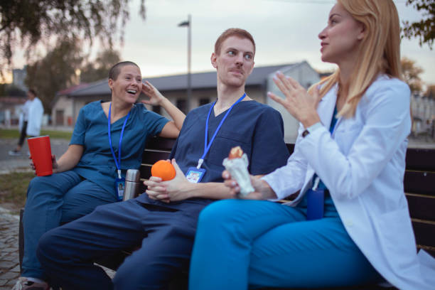 A doctor in a white lab coat talks to her colleagues in uniform, while they sit on a bench stock photo