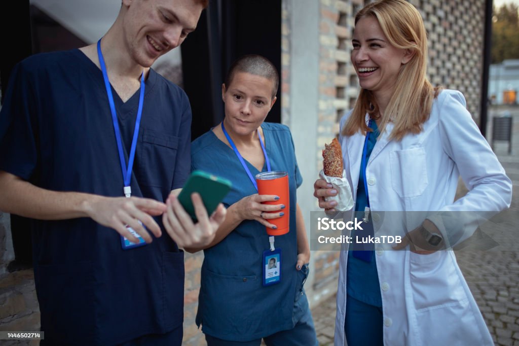 A small group of medical workers are having fun during their lunch break by looking at something on a mobile phone An intern in uniform shows his colleagues something on his mobile phone Nurse Stock Photo