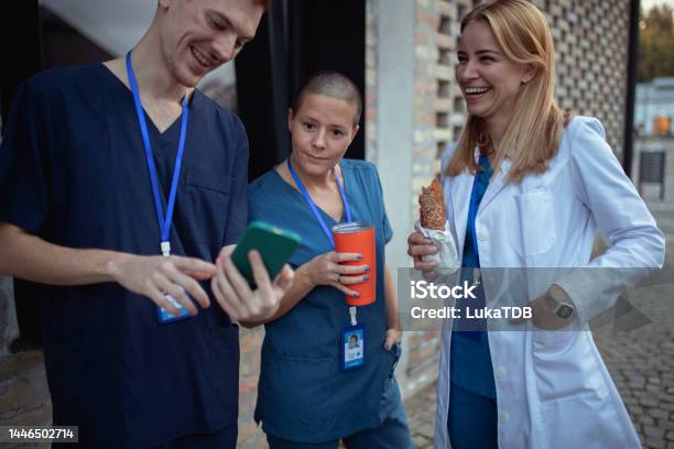 A Small Group Of Medical Workers Are Having Fun During Their Lunch Break By Looking At Something On A Mobile Phone Stock Photo - Download Image Now