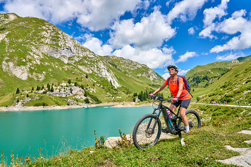 active senior woman, riding her electric mountain bike at Spuller Lake in the Arlberg area near the famous village of Lech, Tirol, Austrian Alps