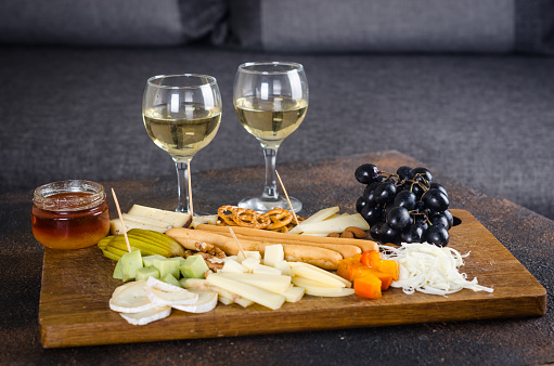 Delicious cheese mix with grapes, jam, snacks, crackers, walnuts and vine on a wooden board. Dinner or aperitif concept. Exquisite cheese plate, wine food.