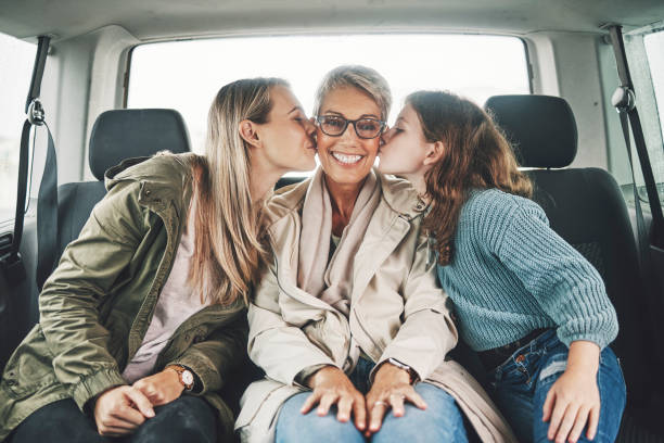 famiglia, bacio e viaggio on the road con una ragazza, madre e nonna sul sedile posteriore di un'auto per un giro. amore, viaggio e trasporto con una donna anziana, figlia e nipote in vacanza o in vacanza - mothers day mother kissing child foto e immagini stock