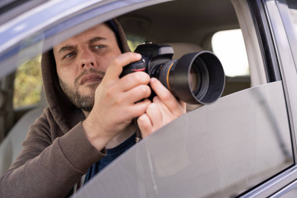 istock Private detective or investigator sitting inside a car doing video surveillance taking pictures with a camera 1446510501