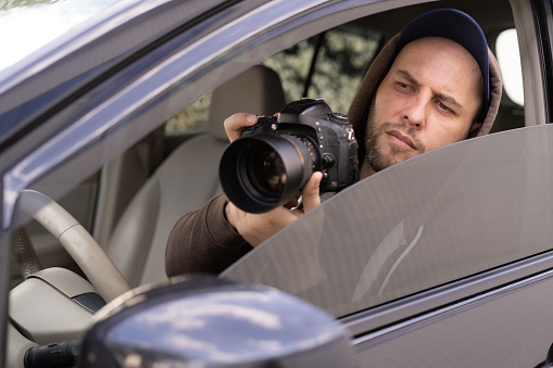 Private detective with camera spying from car, taking photo with professional camera, close up
