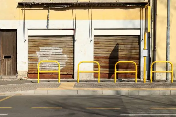 Photo of Abandoned store at the roadside. Sidewalk, bus stop and yellow pedestrian barrier in front.