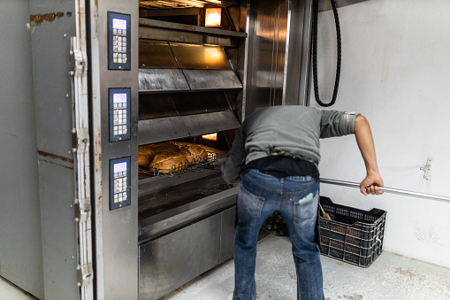 unrecognizable baker taking loaves out of the oven of the artisan bread factory