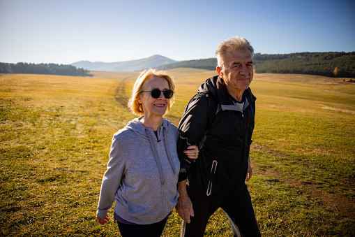 Caucasian senior married couple, holding hands, while enjoying autumn hike, during sunny day