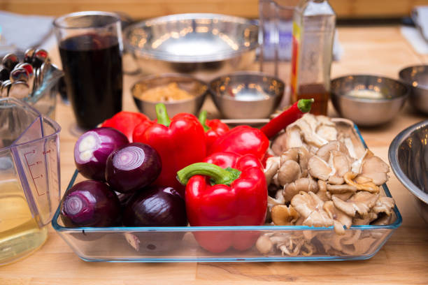 Set of raw red onions, red bell peppers, fresh oyster mushrooms in a glass dish. Kitchen table before cooking. stock photo