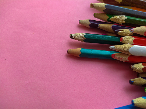 Colored pencils are broken on a pink background. Many different colored pencils. Colored pencil. The pencils are broken. Pencils and a sharpener. Creation. Hobby. Close-up. Copy space. Flat lay