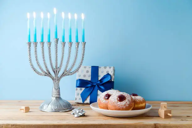Jewish holiday Hanukkah concept with menorah, traditional donuts and gift box on wooden table.