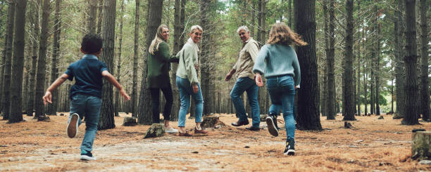 forest, big family and adventure with children, parents and grandparents walking in nature for outdoor hiking, fun and trees on wellness vacation. running kids, travel and happy man and women in woods - vacations two generation family caucasian friendship imagens e fotografias de stock