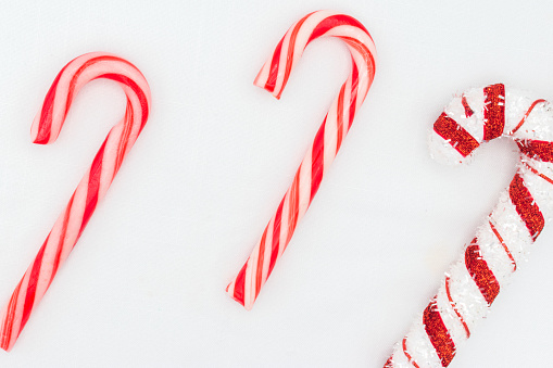 Group of three traditional holiday candy canes in Christmas colours (two red and white, one is a stuffed candy) isolated on a white background.